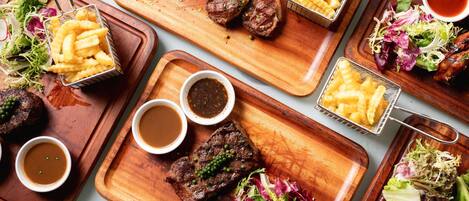 A variety of dishes including steaks, fries, and salads on wooden serving boards.