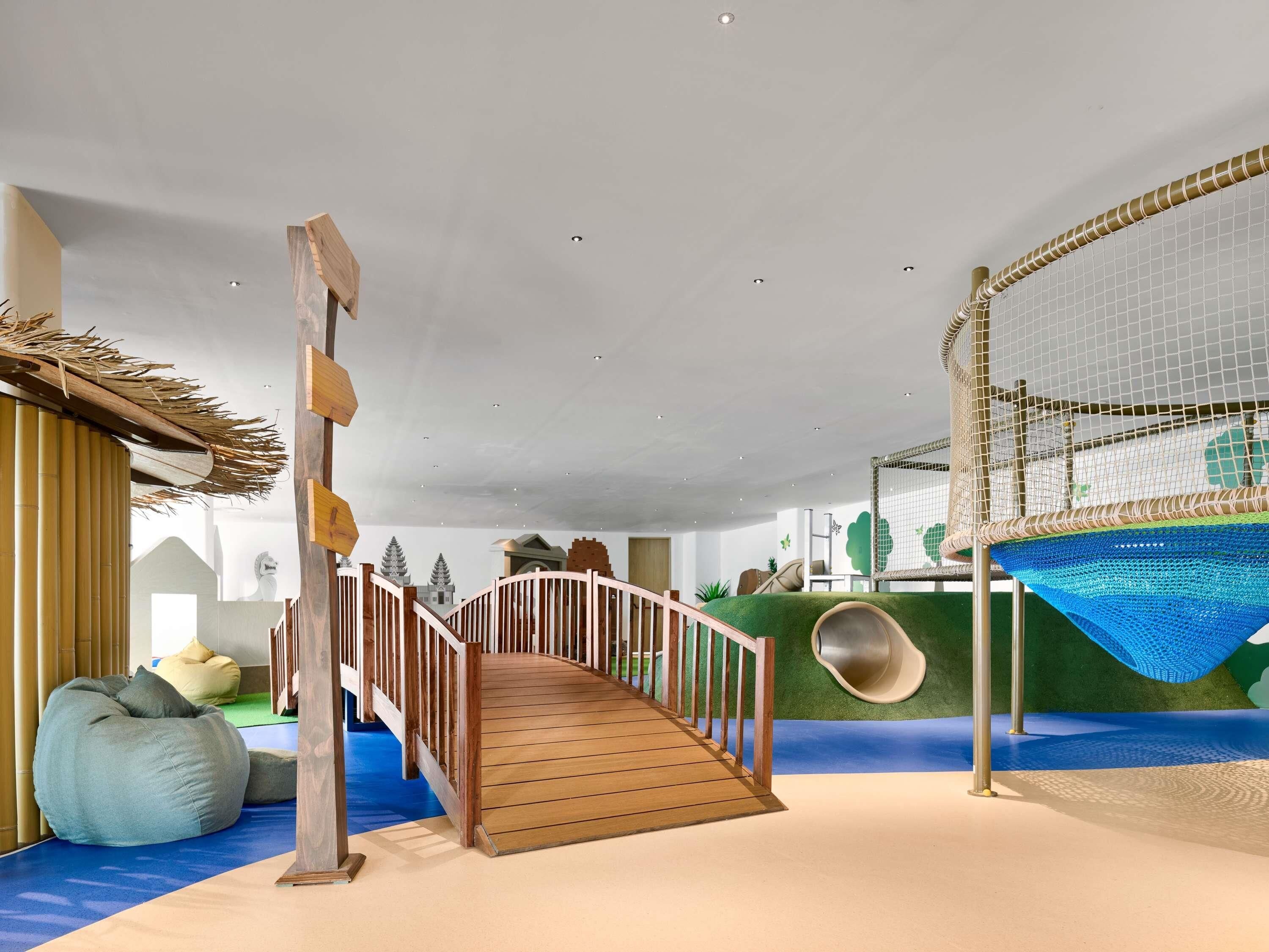 A play area with a wooden bridge, a slide, and a netted climbing structure.