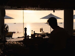 Un bar en la playa con sombrillas, botellas y vasos, con vista al mar.