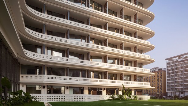 Een meerhoog hotel met balkons op elke verdieping, grote ramen en een verzorgd gazon.
