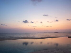 Een rustig zwembad met uitzicht op de oceaan en een zonsondergang.