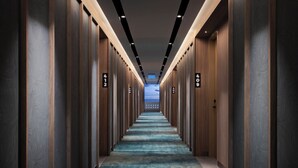 Un pasillo largo y estrecho con paneles de madera y puertas numeradas, que conduce a una habitación luminosa con vista al cielo.