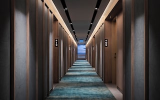 A long, narrow hallway with wooden paneling and numbered doors, leading to a bright room with a view of the sky.