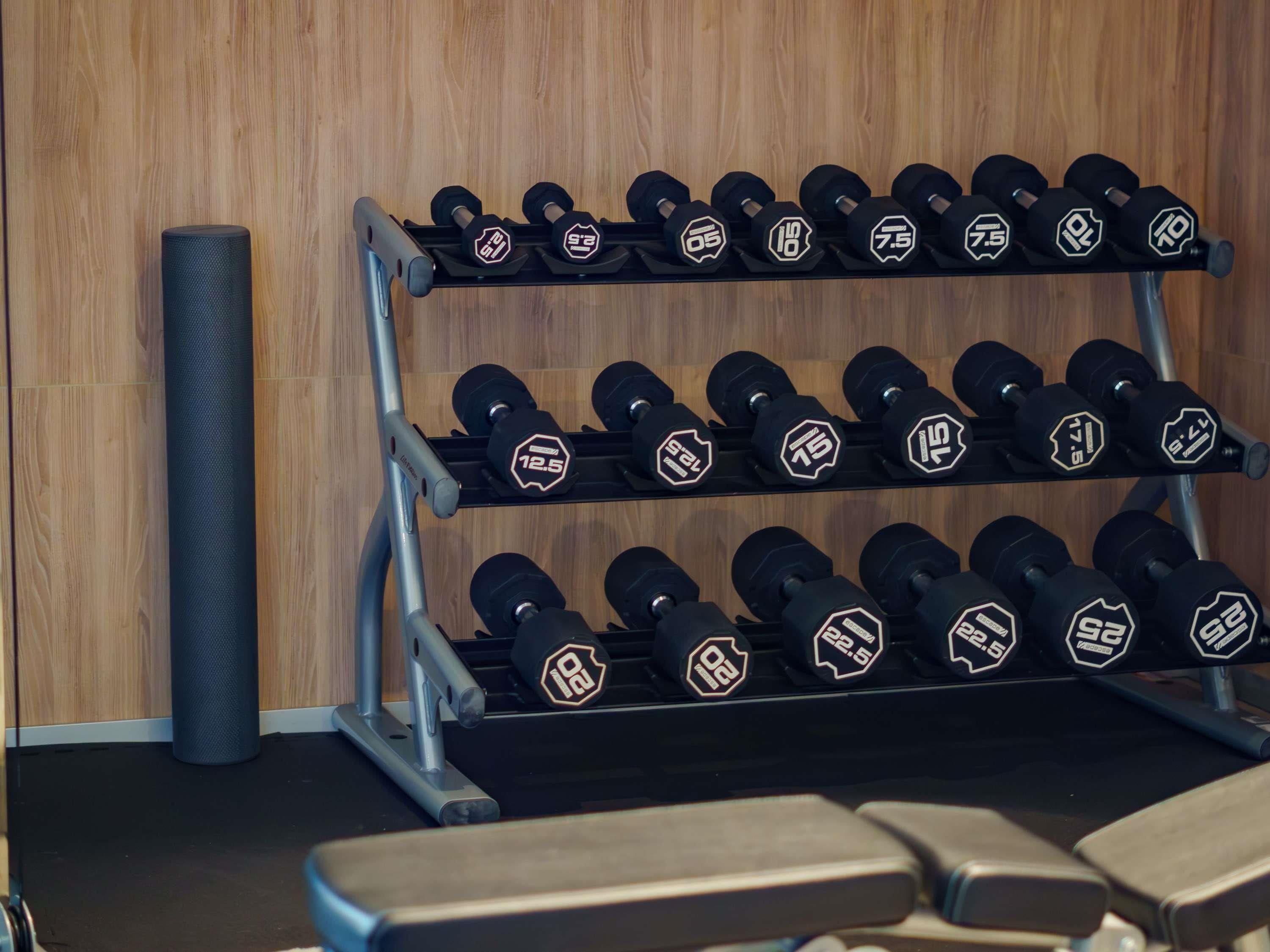 Een sportschool met een rek halters, een yogamat en trainingsbanken.