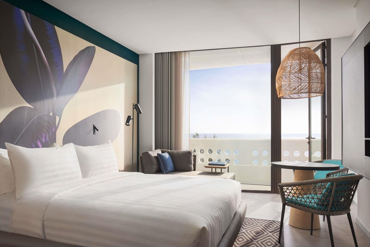 Une chambre d’hôtel comprenant un lit, une chaise, une table, une grande fenêtre avec vue et un élément décoratif mural.
