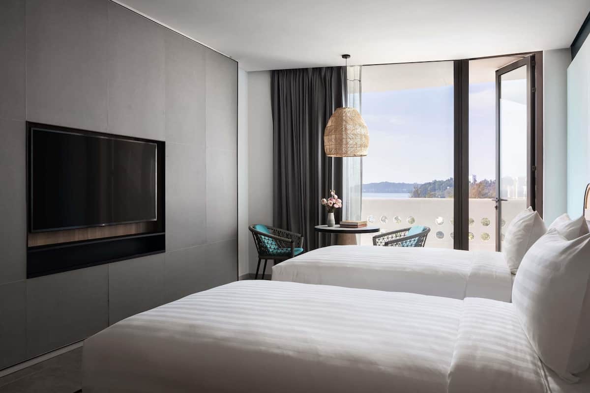 Ett hotellrum med två sängar, en TV, utsikt över staden och en balkong med ett bord och stolar.