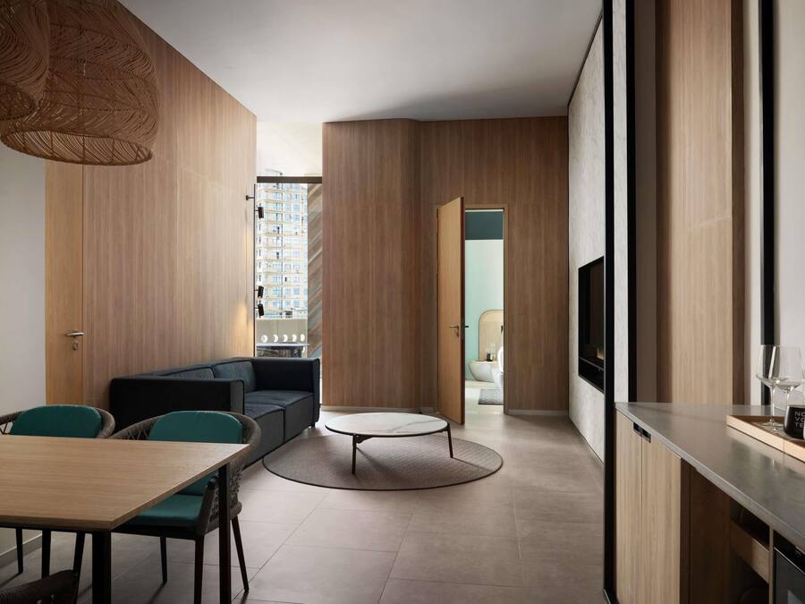 A modern interior with a dining area, sofa, round coffee table, and a kitchen area with a TV.