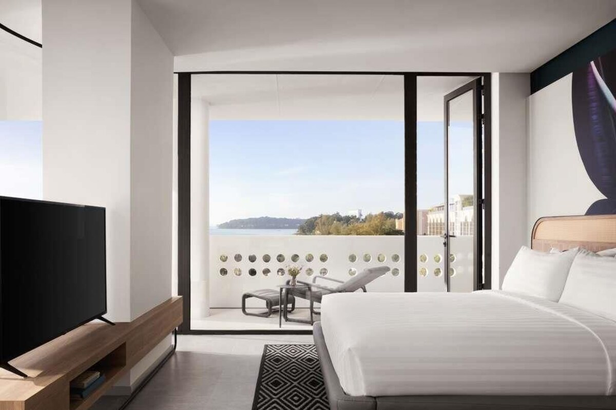 Una habitación de hotel moderna con una cama grande, televisión, balcón con vistas y zona de comedor.