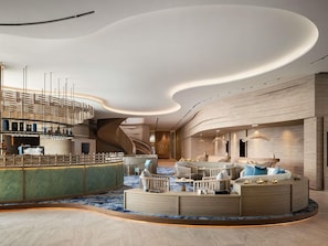 A modern lobby with a curved ceiling, a central seating area with sofas and chairs, a bar area with a counter, and a staircase leading to an upper level. - Novotel Sihanoukville Holiday Resort (Sihanoukville)