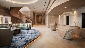 Un moderno vestíbulo de hotel con una zona de estar curva, una recepción y una escalera.