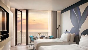 Una habitación de hotel con dos camas, un televisor, un balcón con vistas a la puesta de sol y una mesa con sillas.