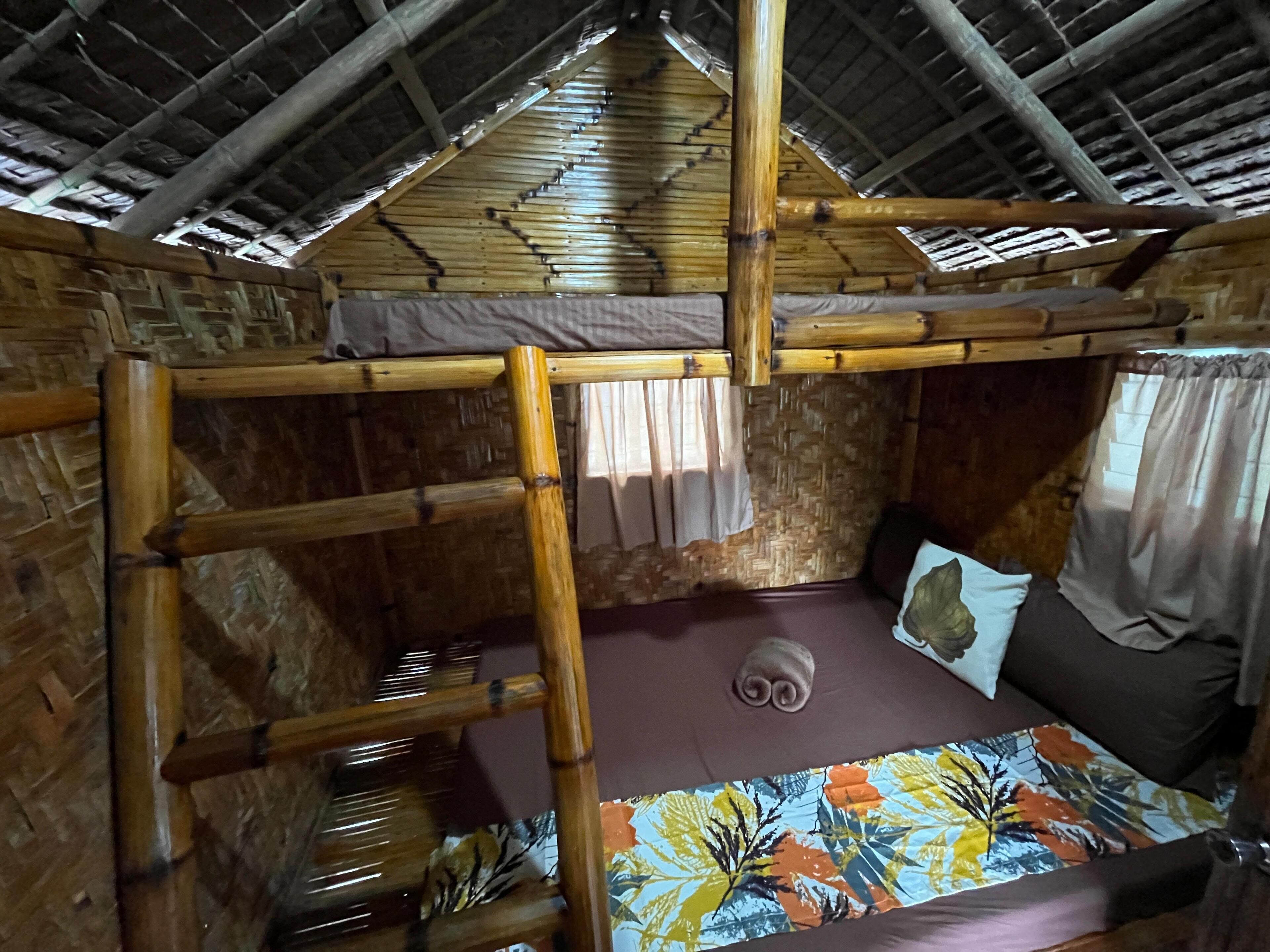 A rustic wooden room with a high ceiling, a bed with a colorful floral bedspread, and a small painting on the wall.