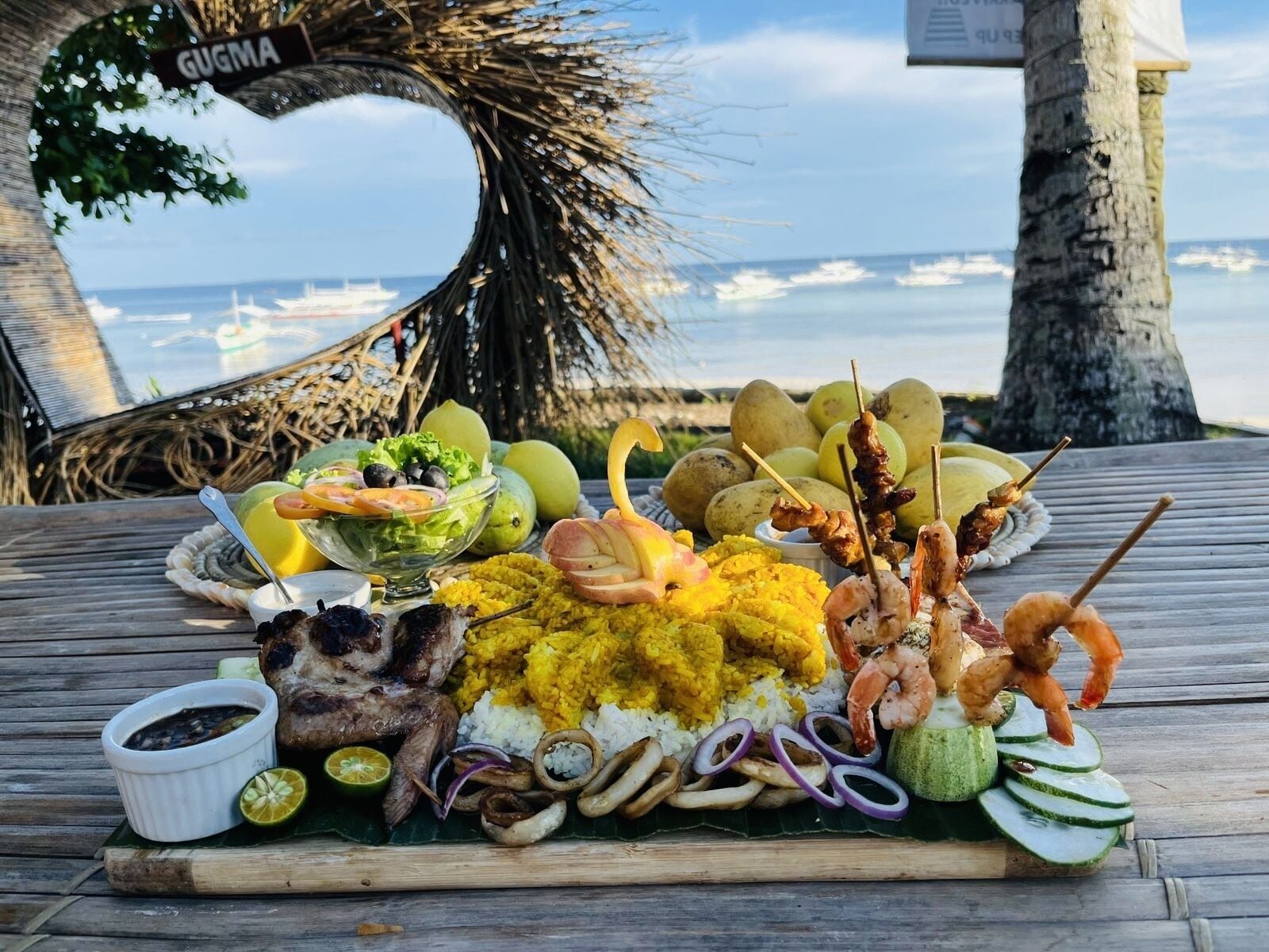 A seafood platter with rice, shrimp, and other items on a wooden table with a view of the ocean.
