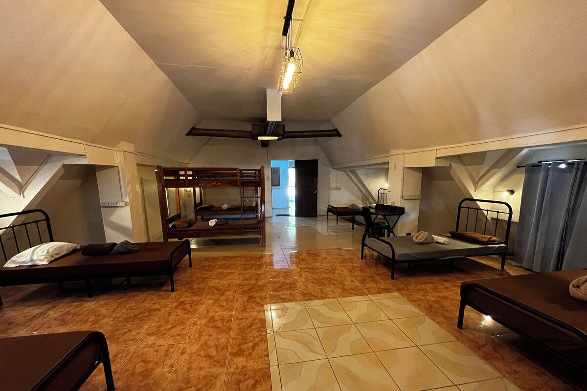 Amplia habitación en ático con literas, una mesa de comedor y una escalera que sube a un nivel superior.