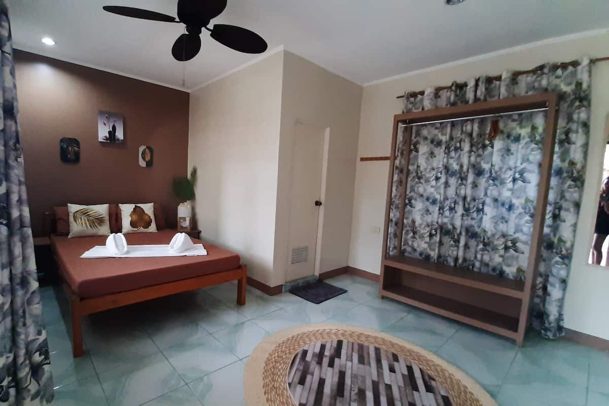 A bedroom with a bed, a ceiling fan, a door, and a window with curtains.