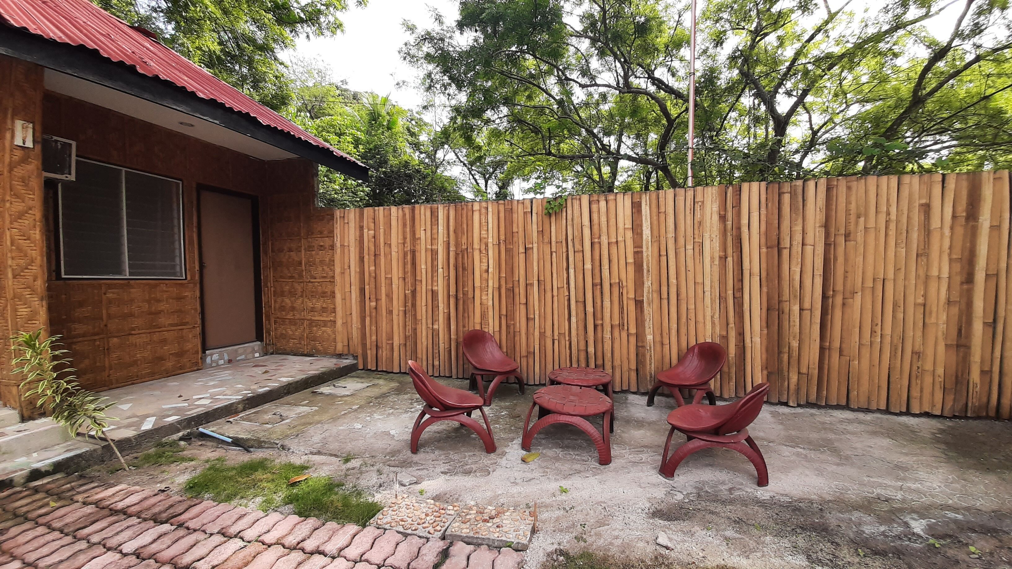 A patio with a wooden fence, a small building with a red roof, and red plastic chairs and tables.