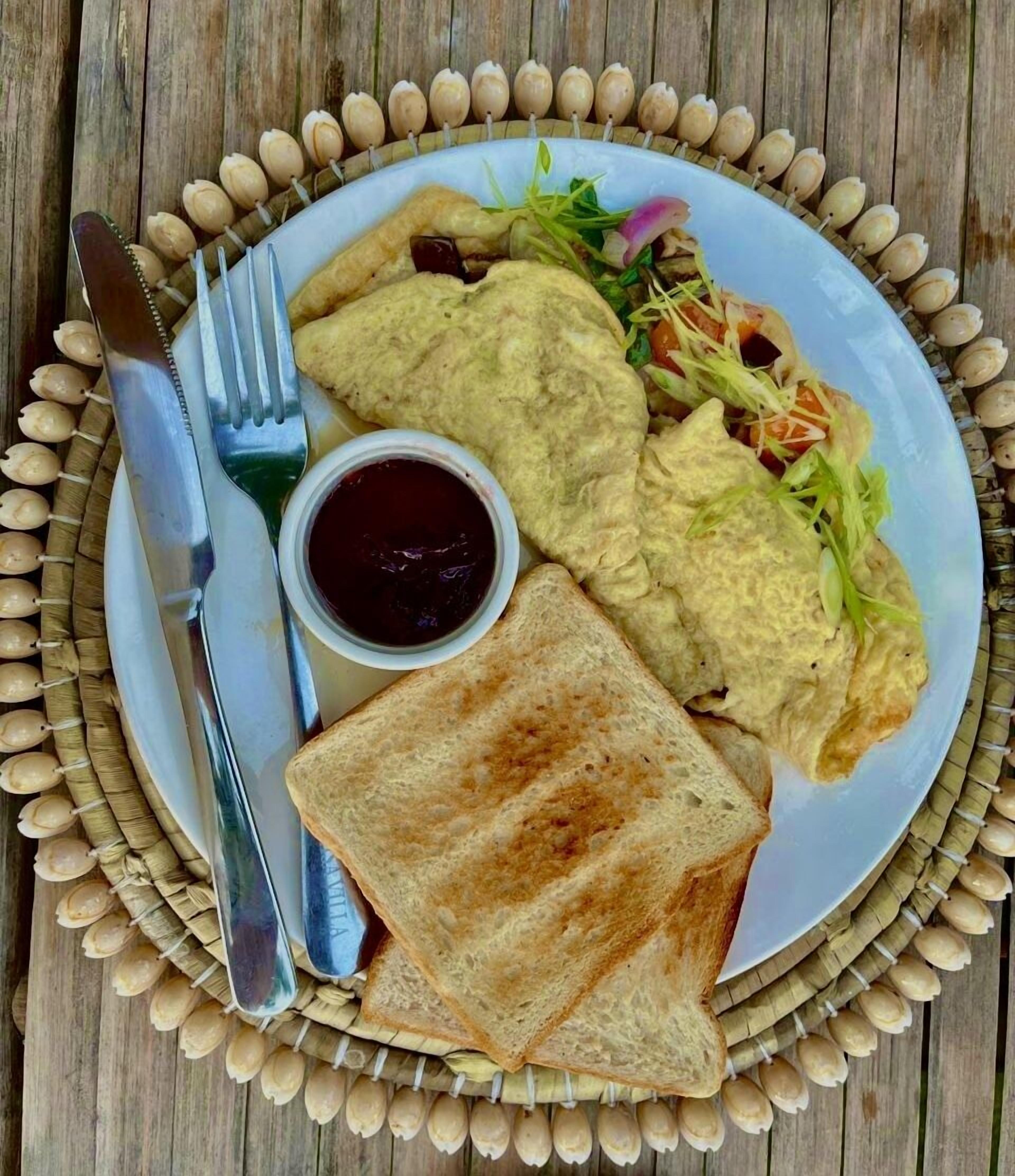A plate with toast, scrambled eggs, and a side salad, accompanied by a fork and knife on a wooden table.