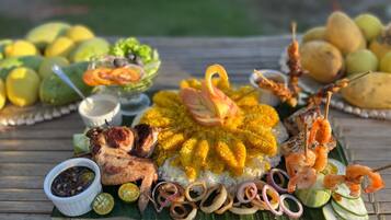 A table with a variety of dishes including rice, grilled meat, shrimp, and vegetables.