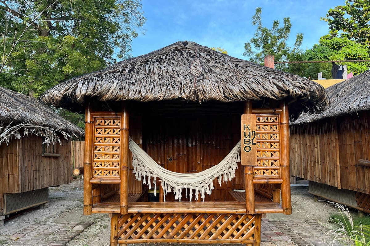 A thatched-roof hut with a hammock, wooden lattice walls, and a sign reading "KUBO".