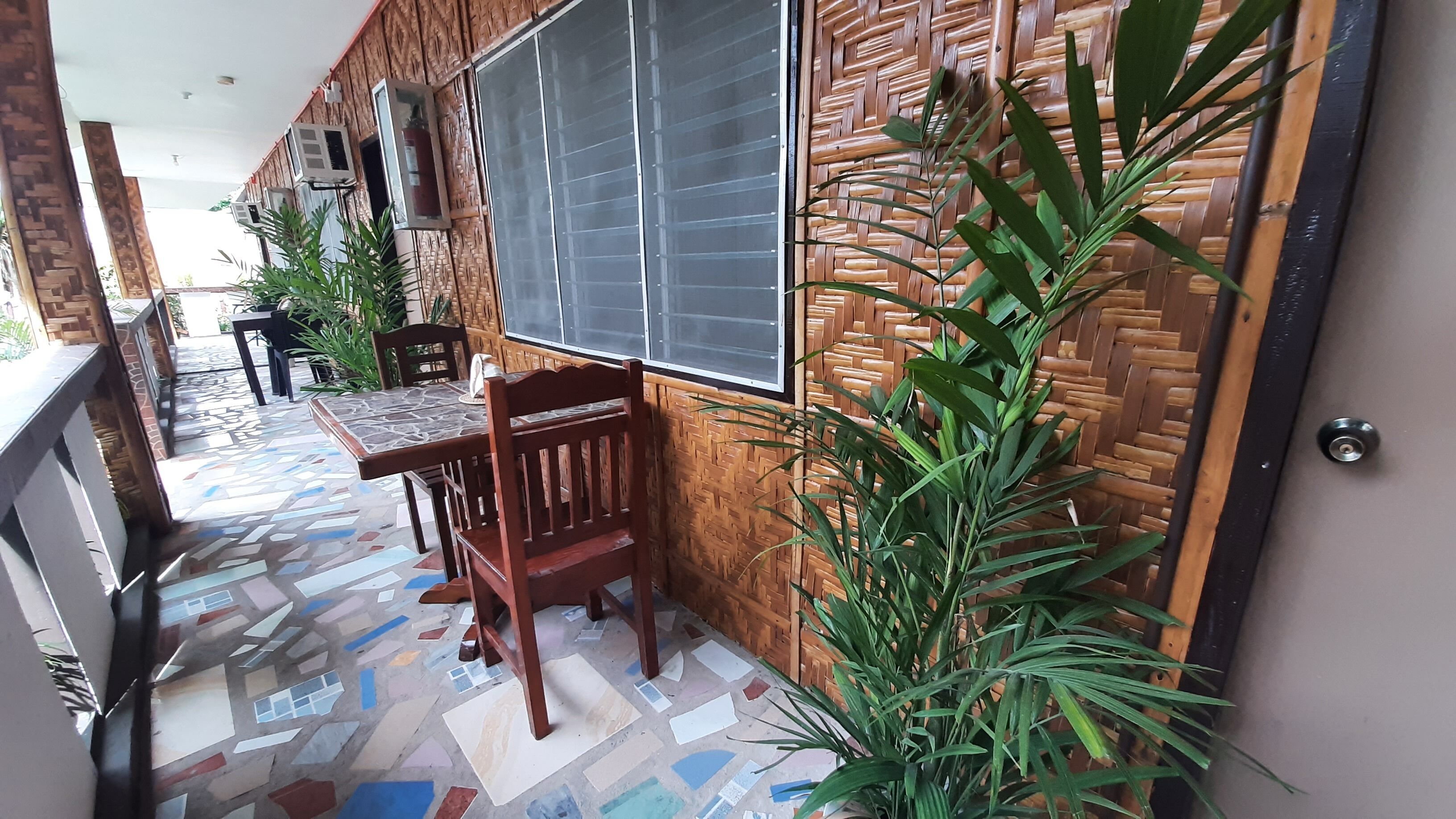 A covered outdoor area with a tiled floor, a table with chairs, and a large window.
