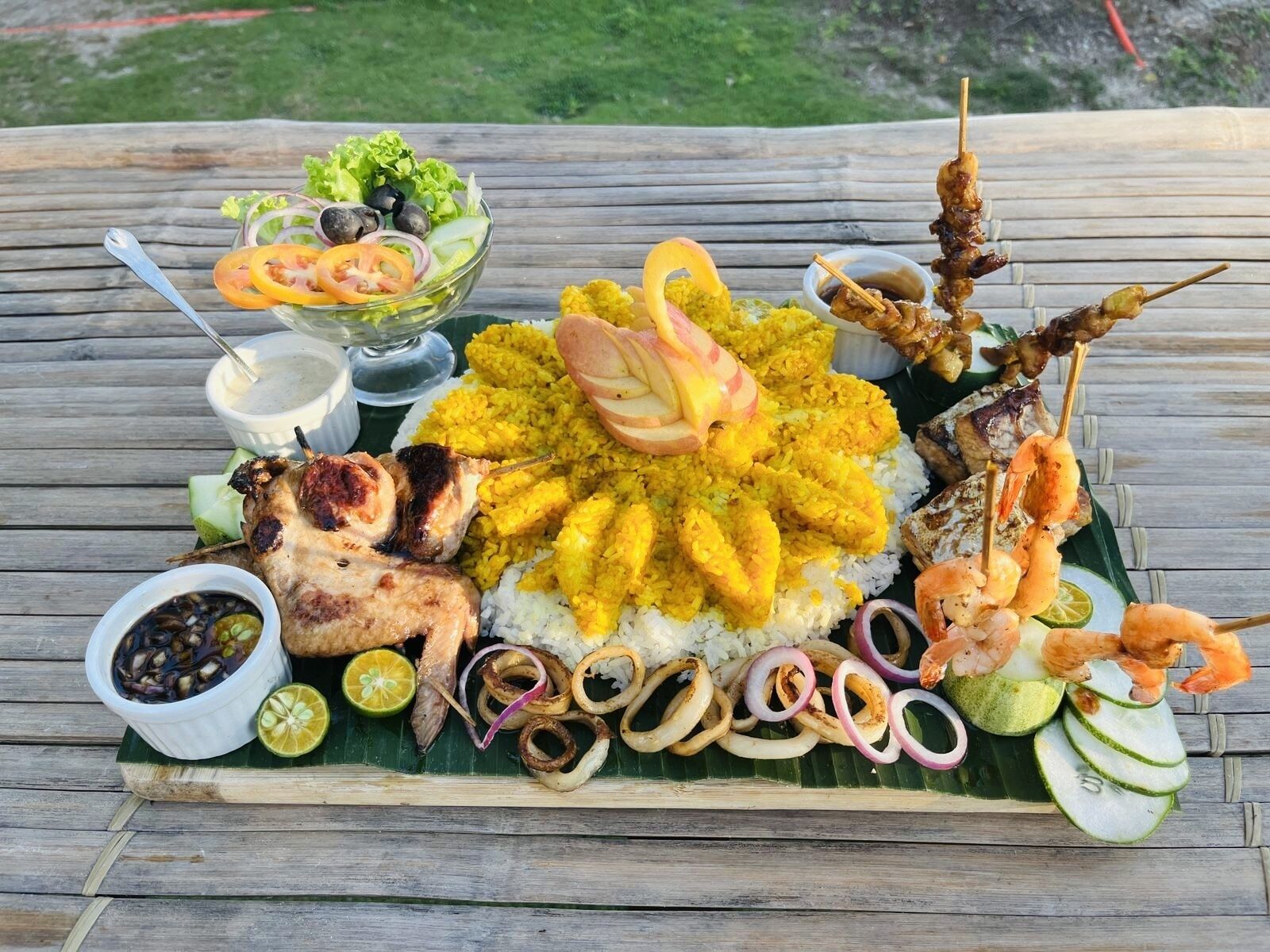 Une table en bois sur laquelle on trouve une variété d’aliments, notamment de la viande grillée, du riz, des crevettes et des légumes.