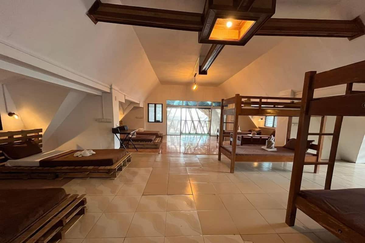A spacious loft bedroom with a high ceiling, a bunk bed, a desk, and a large window providing natural light.