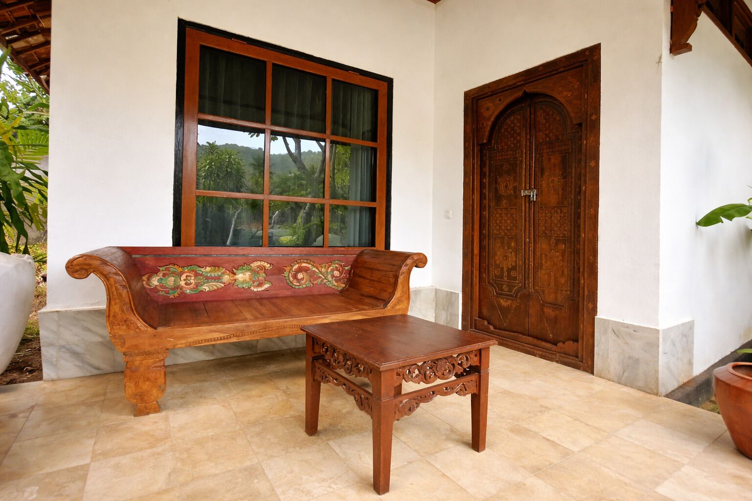 A wooden bench and table set against a white wall with a large window and a wooden door.