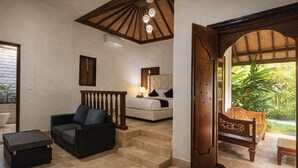 A room with a bed, a sofa, a coffee table, and a wooden chair. There is a staircase leading to another level.