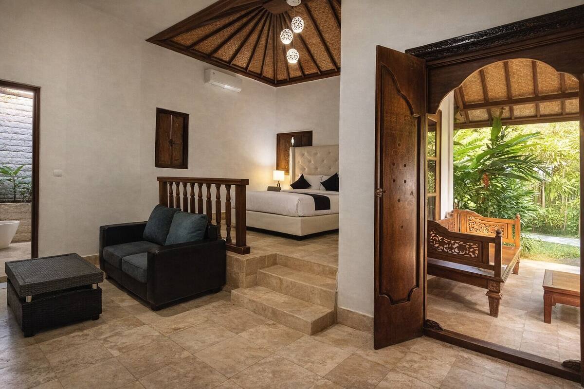 A room with a bed, a sofa, a coffee table, and a wooden chair. There is a staircase leading to another level.