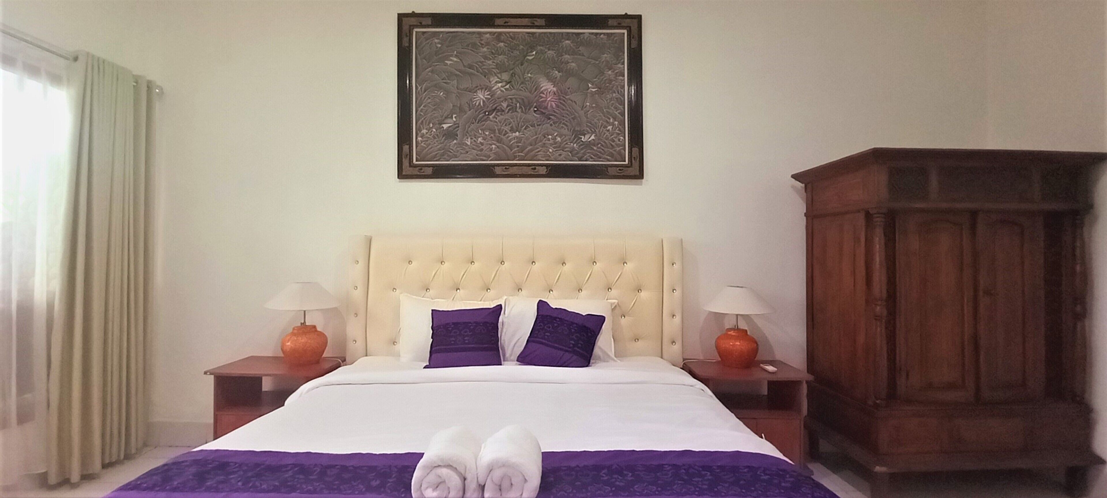 A hotel room with a large bed, two nightstands, a wooden cabinet, and a framed artwork on the wall.