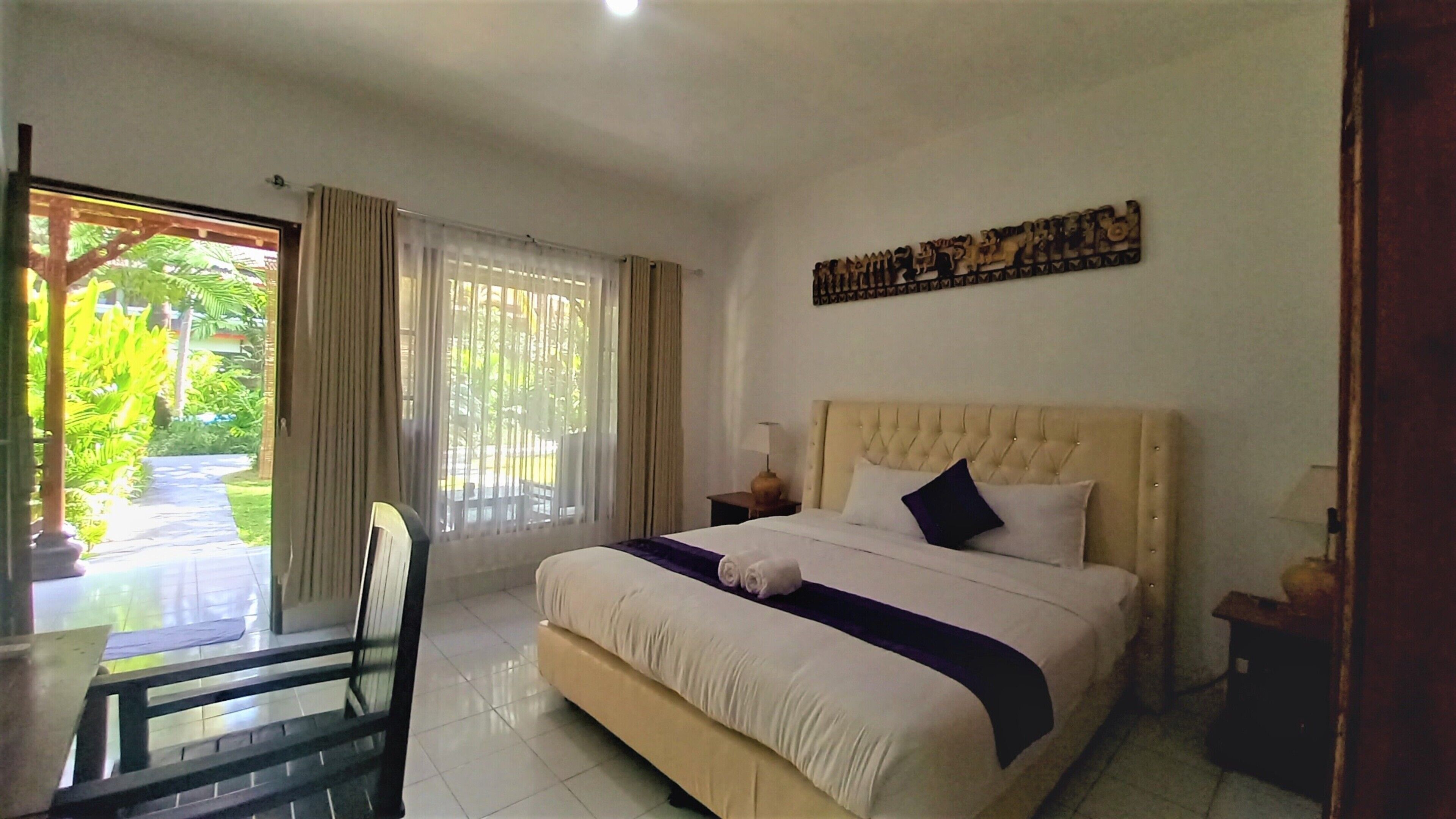 A hotel room with a bed, a chair, a desk, and a window with curtains.