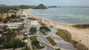 A coastal area with a beach, a promenade, and a small hill in the background.