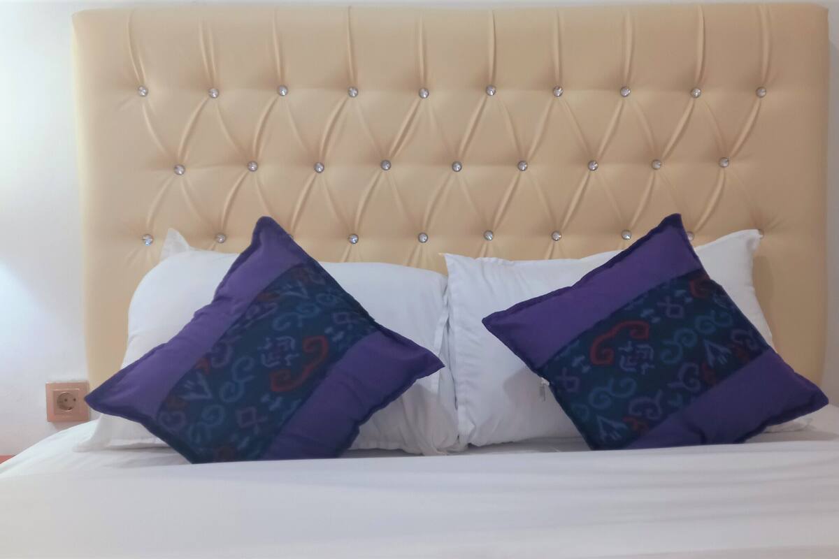 A bed with a tufted headboard, two white pillows, and two patterned pillows.
