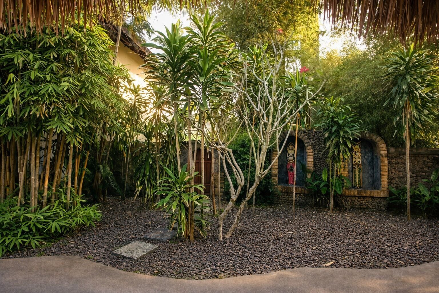A garden with bamboo, a stone statue, and a thatched roof structure.