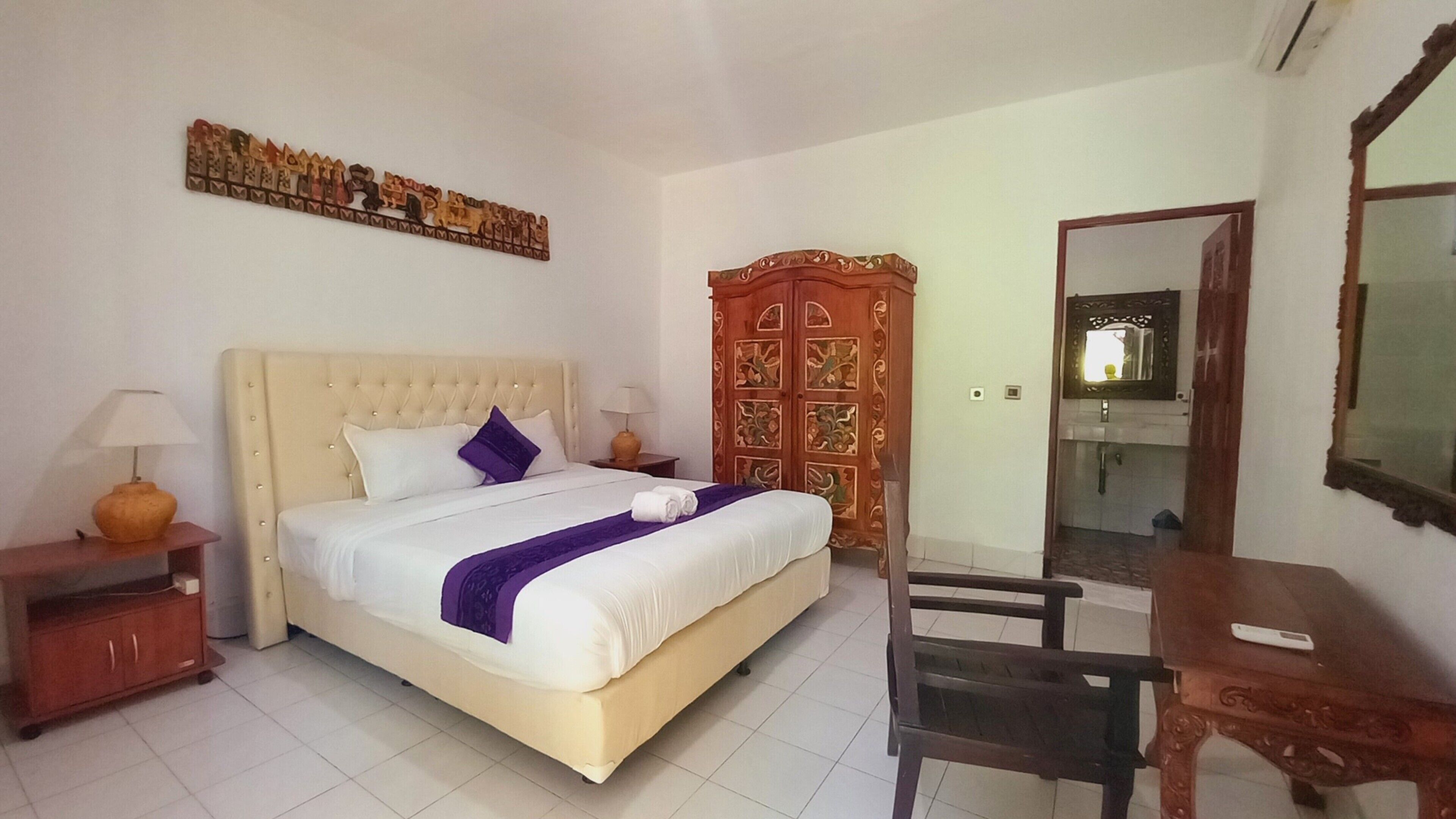 A hotel room with a large bed, a wooden wardrobe, a desk, and a mirror.