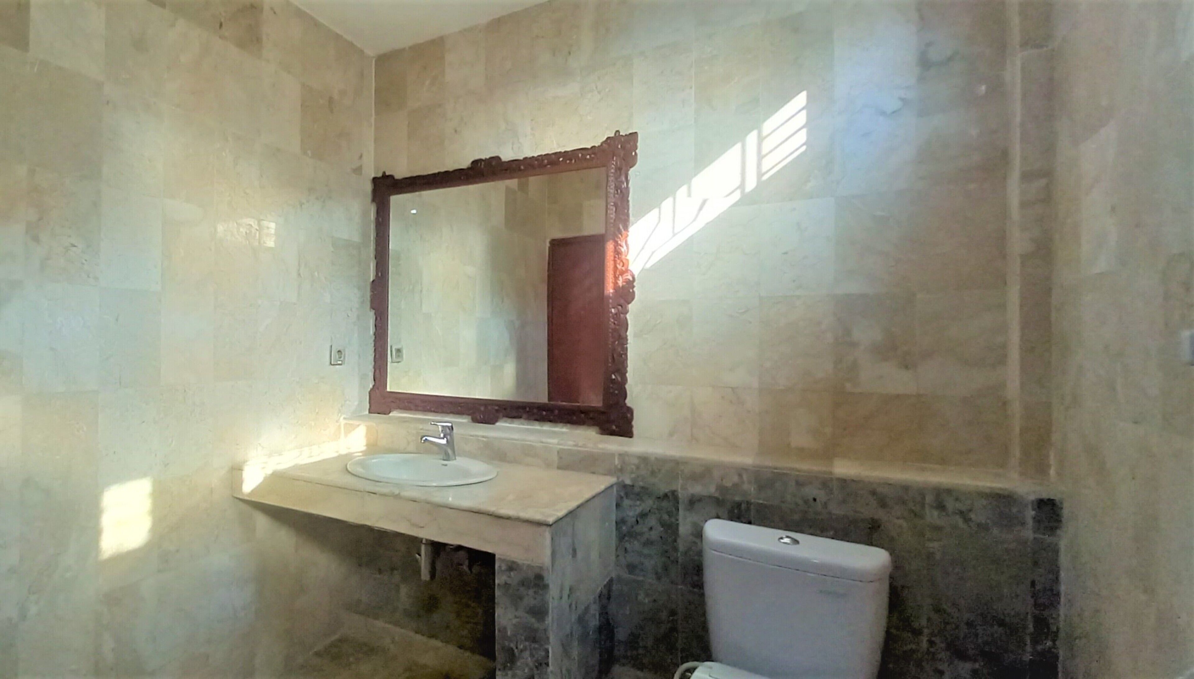 A bathroom with a marble wall, a sink with a mirror, and a toilet.