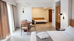 A hotel room with a bed, a desk with a chair, a table with a bottle, and a wardrobe. - Alexandra Beach Hotel (Chania)