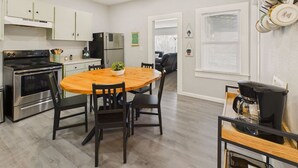 A modern kitchen with a wooden dining table, black chairs, stainless steel appliances, and a coffee maker. - Single Family Home with Fenced Backyard and AC! (Philomath)