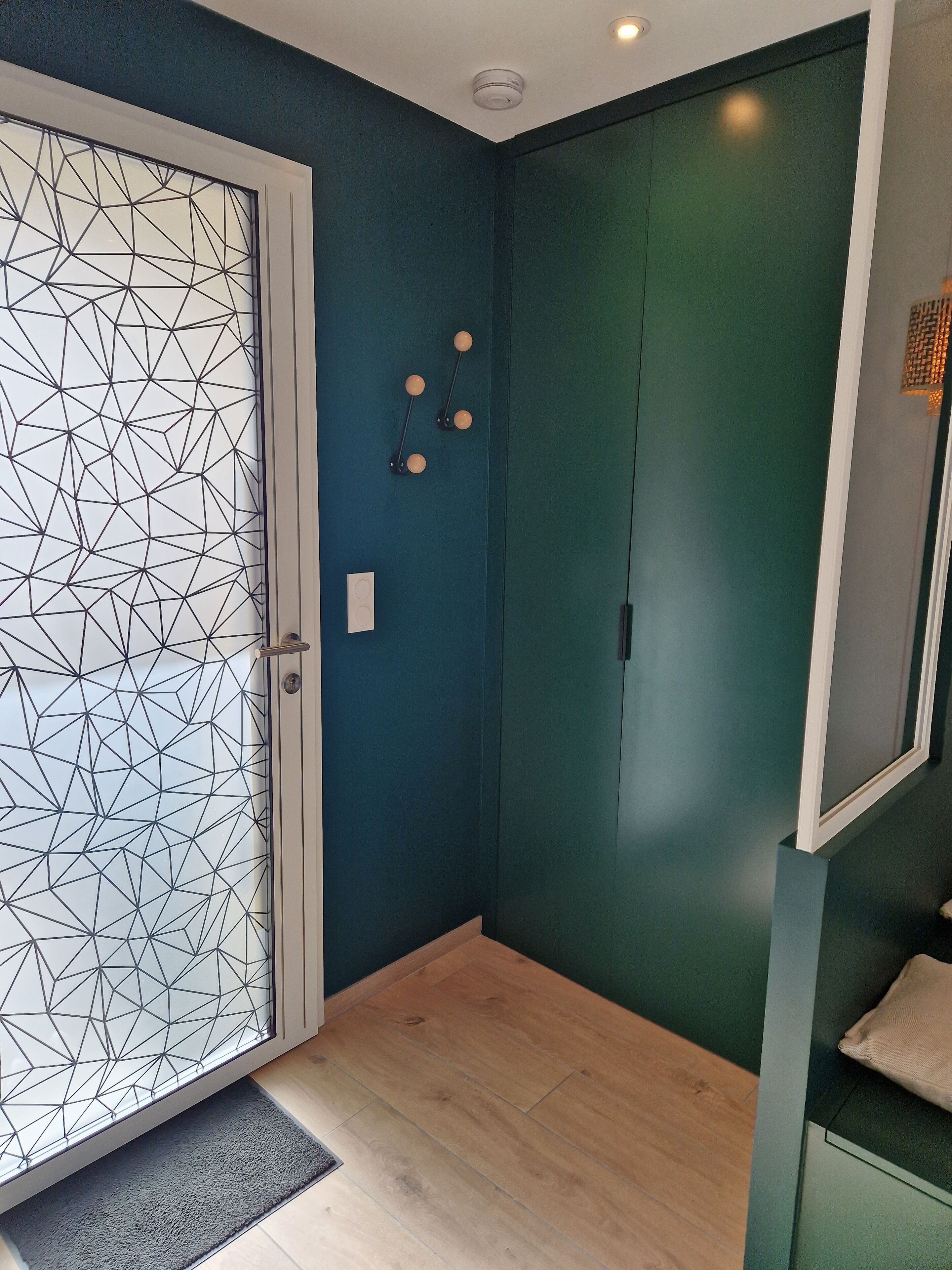 A room with a geometric patterned door, a teal wall, a wooden floor, and a small rug.
