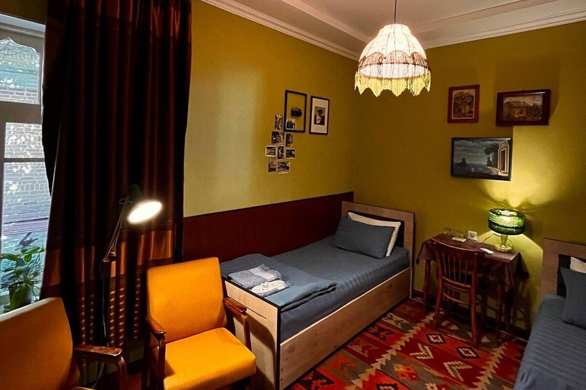 Una habitación pequeña con una cama individual, una mesita, una silla y una lámpara colgante.