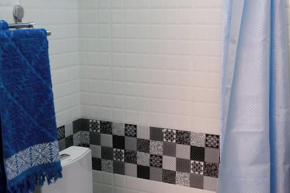 A bathroom with white tiled walls, a patterned tile border, a toilet, and a blue towel.
