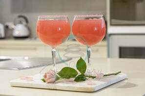 Twee glazen roze drank op een marmeren onderzetter met een roos en bladeren.