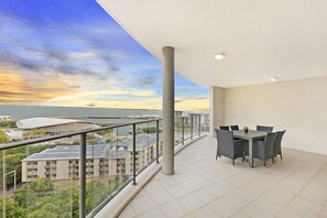 Een balkon met een tafel en stoelen, met uitzicht op water en gebouwen.