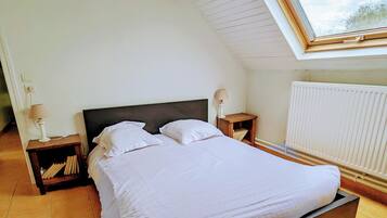 A bedroom with a large bed, wooden headboard, two bedside tables with lamps, a window with a view, and a radiator.