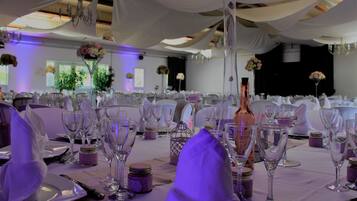 A banquet hall with tables set for a formal event, featuring white tablecloths, glassware, and floral centerpieces.
