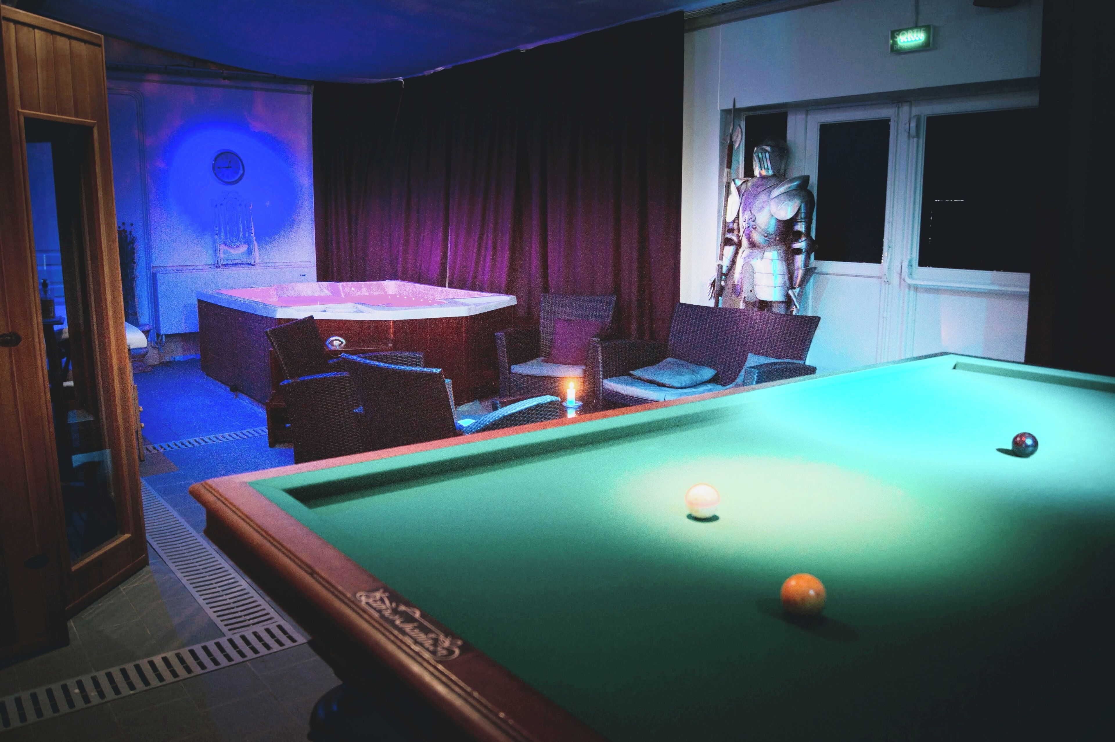 A pool table with balls, a clock on the wall, and a statue.
