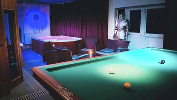 A pool table with balls, a clock on the wall, and a statue.