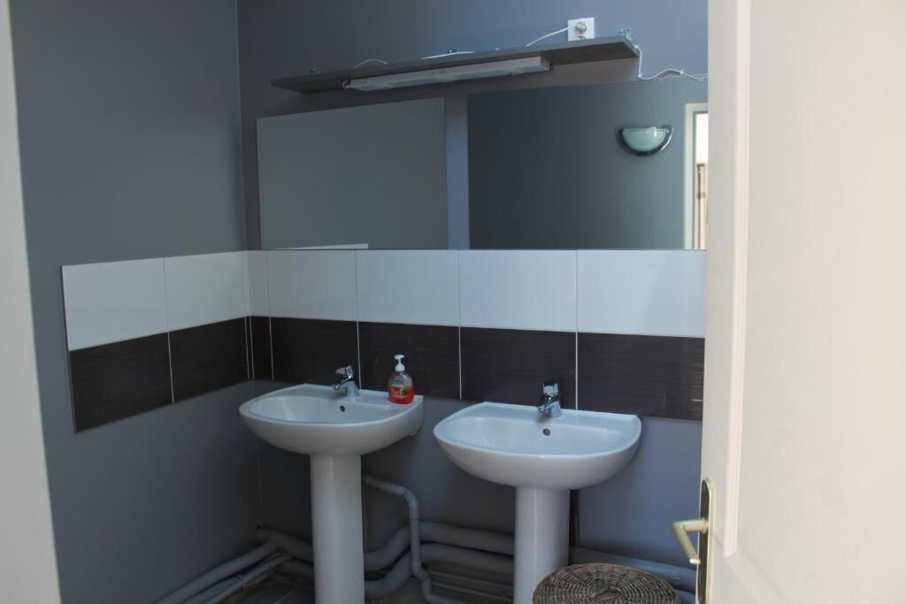 Un bagno con due lavandini bianchi, uno specchio sopra e uno scaffale con una lampada.