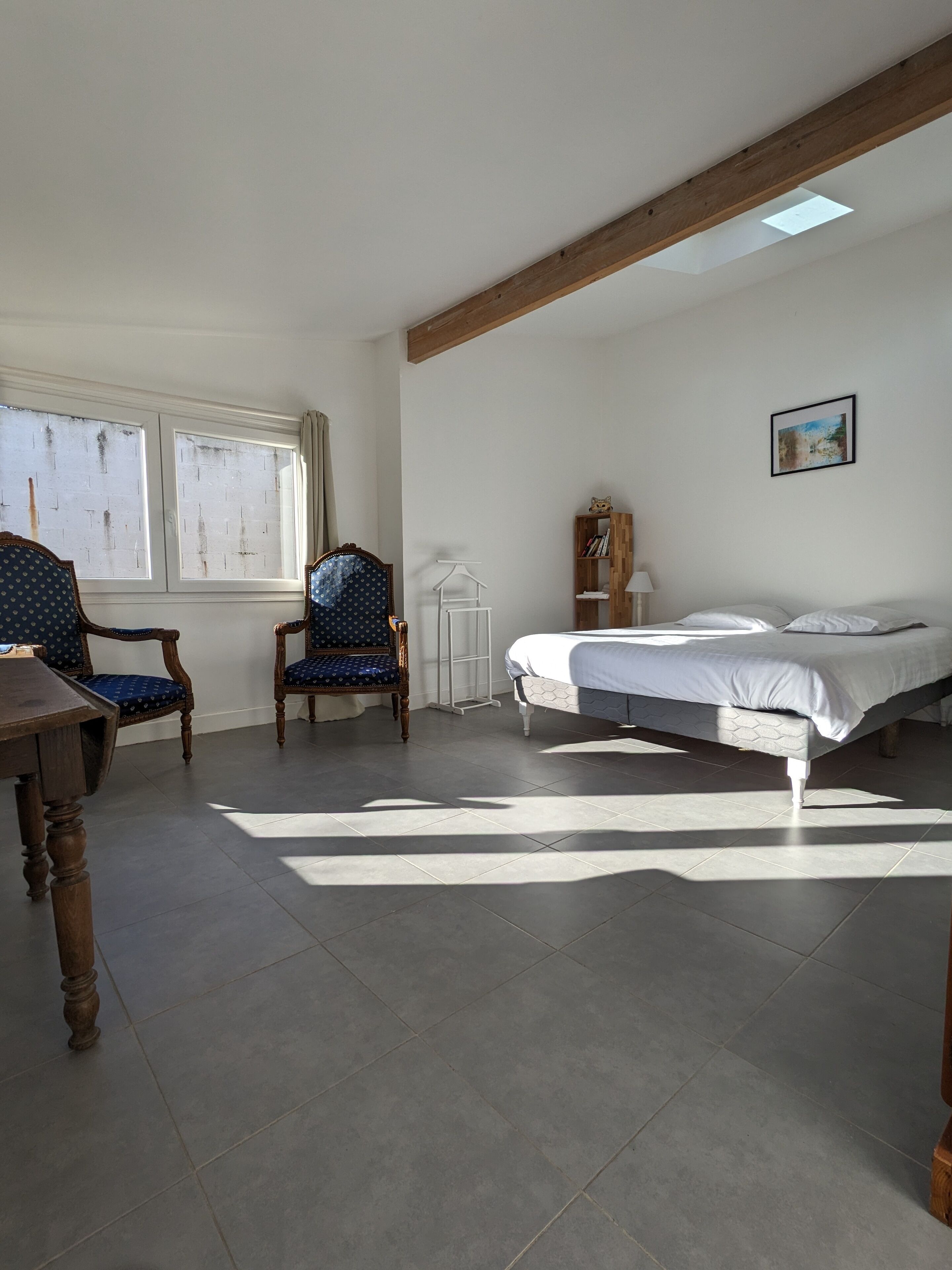 Un dormitorio con una cama, dos sillas, un armario de madera y una ventana con cortinas.
