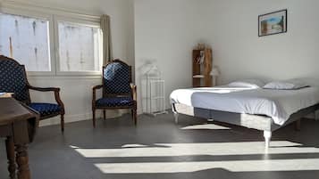 Un dormitorio con una cama, dos sillas, un armario de madera y una ventana con cortinas.